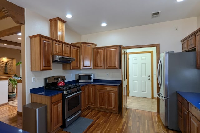 kitchen featuring visible vents, dark wood finished floors, stainless steel appliances, under cabinet range hood, and brown cabinets