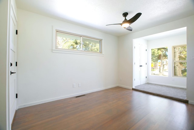 empty room featuring baseboards, dark wood-type flooring, a healthy amount of sunlight, and a ceiling fan