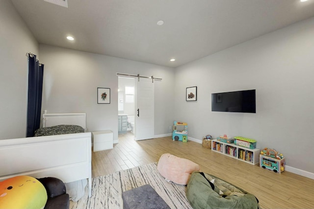 bedroom with wood finished floors, baseboards, recessed lighting, a barn door, and connected bathroom