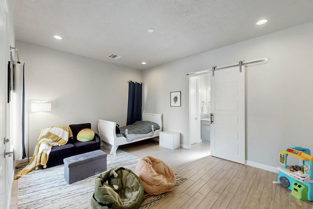 bedroom featuring visible vents, baseboards, recessed lighting, a barn door, and light wood-type flooring