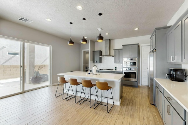 kitchen with a breakfast bar area, gray cabinetry, decorative backsplash, light wood-style floors, and wall chimney exhaust hood