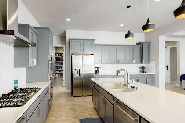 kitchen with gray cabinets, a sink, stainless steel appliances, light countertops, and wall chimney exhaust hood