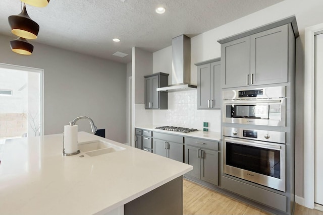 kitchen featuring tasteful backsplash, gray cabinetry, wall chimney range hood, appliances with stainless steel finishes, and a sink