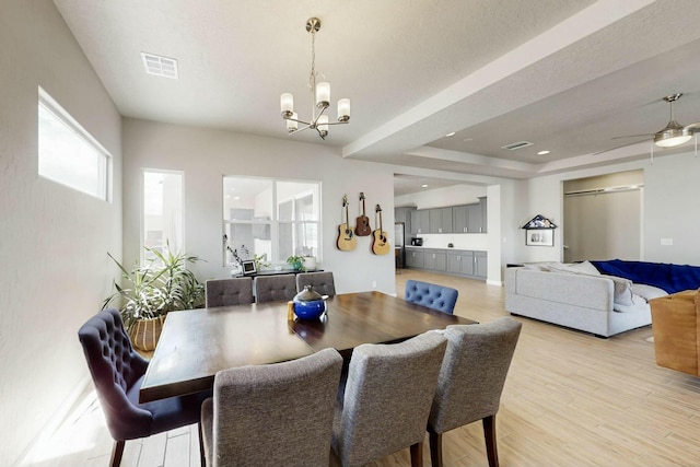 dining area featuring visible vents, a raised ceiling, a chandelier, and light wood finished floors