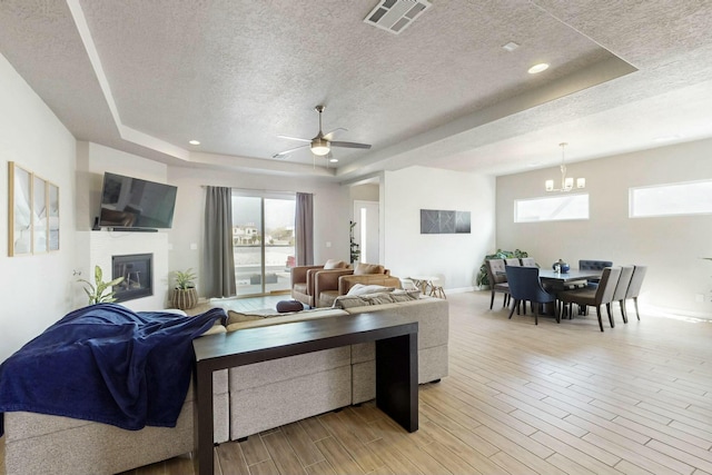 living area with visible vents, light wood-style flooring, a textured ceiling, and a tray ceiling