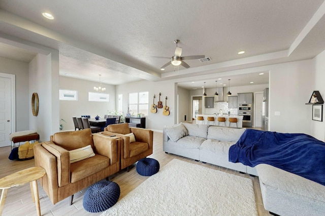 living area featuring light wood finished floors, recessed lighting, ceiling fan with notable chandelier, and a tray ceiling