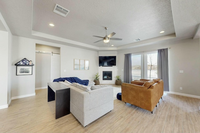 living room with a barn door, visible vents, light wood-type flooring, and a tray ceiling