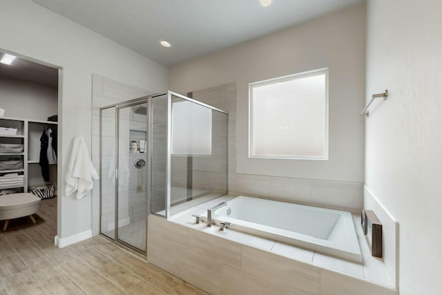 bathroom featuring wood finish floors, a stall shower, a walk in closet, and a garden tub