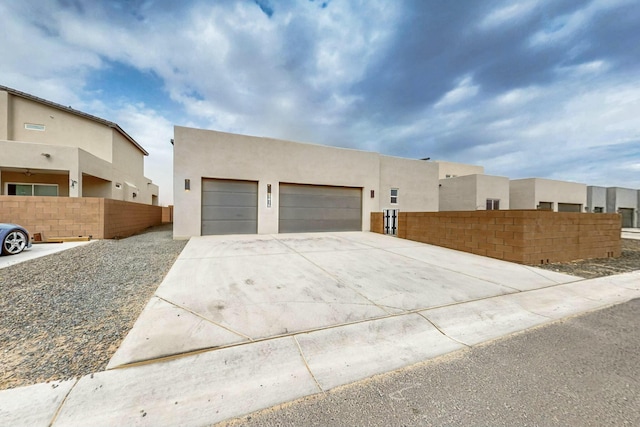 view of front facade with stucco siding, a garage, concrete driveway, and fence