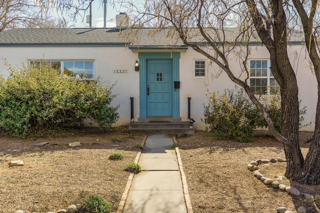 doorway to property with a shingled roof, a chimney, and stucco siding