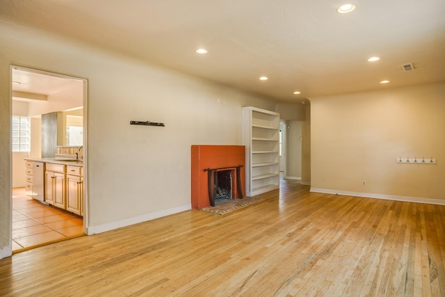 unfurnished living room featuring a fireplace with raised hearth, visible vents, light wood-style flooring, and recessed lighting