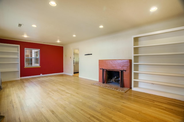 unfurnished living room with recessed lighting, a fireplace, built in features, and light wood-style floors