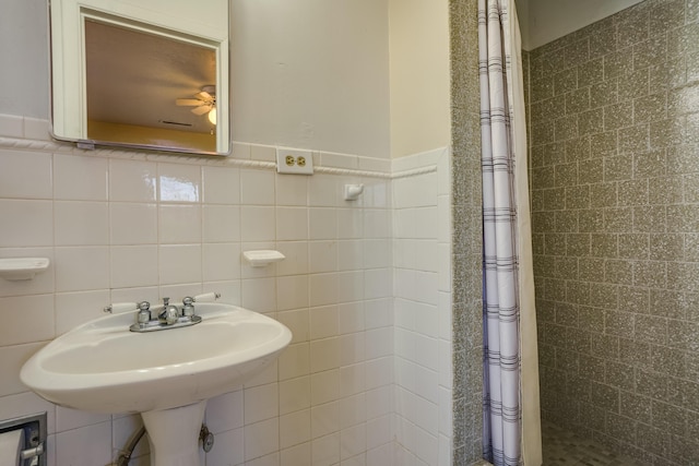 bathroom featuring a sink, a wainscoted wall, a tile shower, and tile walls