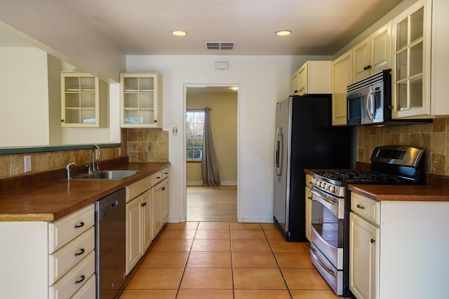 kitchen with visible vents, dark countertops, stainless steel appliances, a sink, and light tile patterned flooring