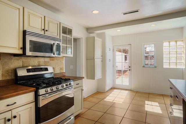 kitchen with appliances with stainless steel finishes, dark countertops, cream cabinetry, and visible vents