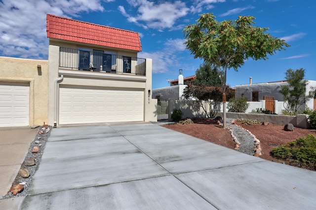 view of front facade featuring a tile roof, stucco siding, concrete driveway, fence, and a balcony