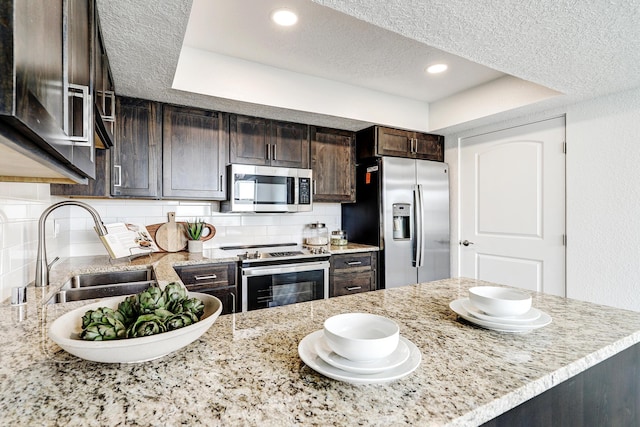 kitchen featuring dark brown cabinetry, tasteful backsplash, stainless steel appliances, a textured ceiling, and a sink