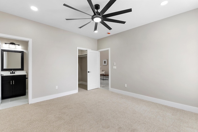 unfurnished bedroom with a walk in closet, recessed lighting, light carpet, a sink, and baseboards