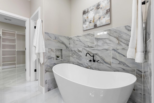 bathroom with visible vents, a soaking tub, marble finish floor, a walk in closet, and tile walls