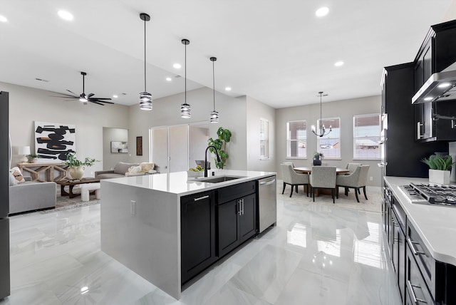 kitchen with a sink, light countertops, appliances with stainless steel finishes, dark cabinetry, and a center island with sink