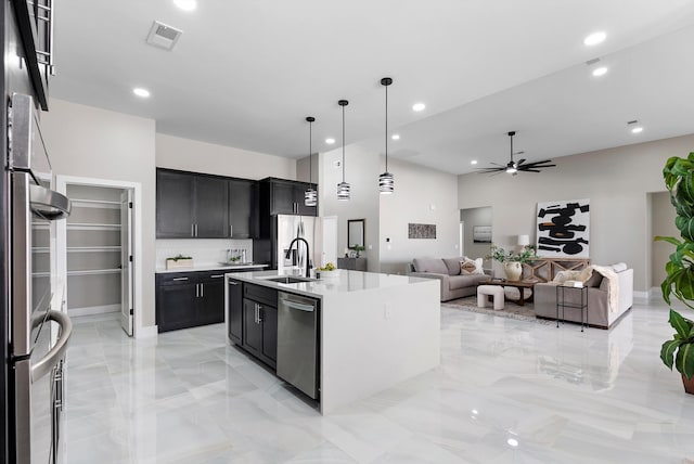 kitchen with a sink, a ceiling fan, light countertops, appliances with stainless steel finishes, and dark cabinetry