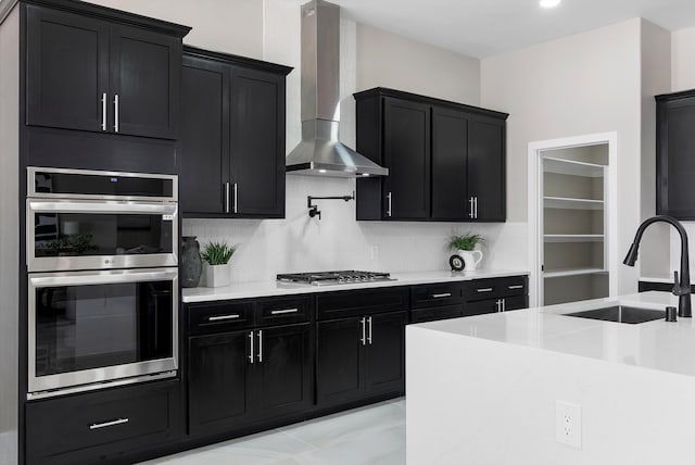 kitchen with a sink, wall chimney exhaust hood, stainless steel appliances, and dark cabinets