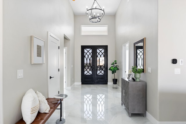 foyer with a notable chandelier, a towering ceiling, baseboards, marble finish floor, and french doors