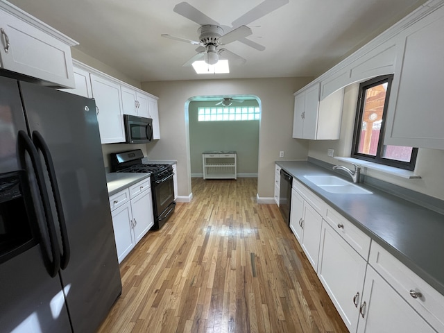 kitchen featuring light wood-style flooring, a sink, white cabinetry, heating unit, and black appliances