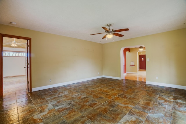 empty room with stone finish floor, ceiling fan, arched walkways, and baseboards