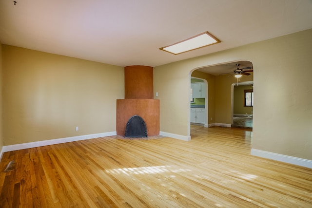 unfurnished living room with a ceiling fan, baseboards, arched walkways, and wood finished floors