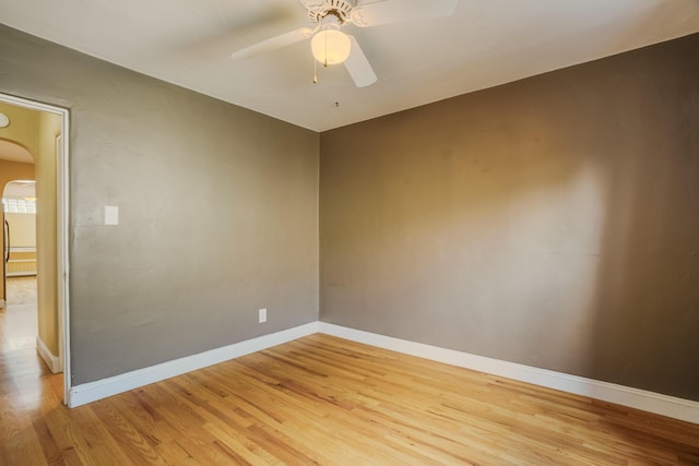 empty room featuring arched walkways, ceiling fan, baseboards, and light wood-style floors