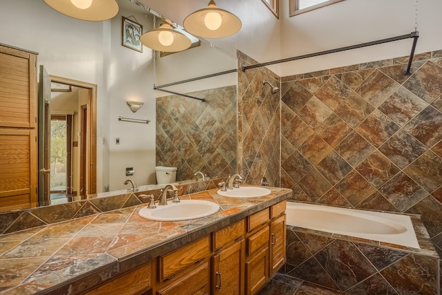 bathroom with tiled shower / bath, double vanity, a sink, and toilet