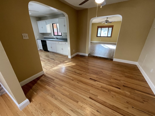 unfurnished dining area with arched walkways, light wood-type flooring, a ceiling fan, and baseboards