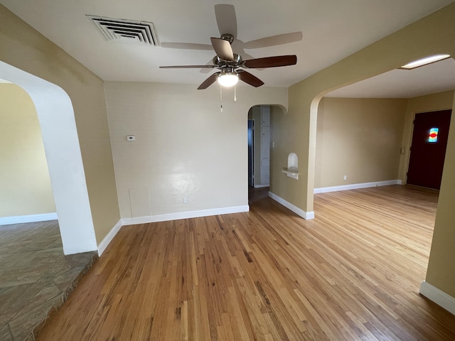 empty room with arched walkways, wood finished floors, visible vents, and baseboards