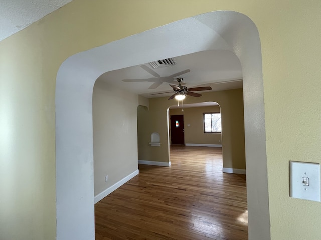 corridor with visible vents, baseboards, arched walkways, and wood finished floors