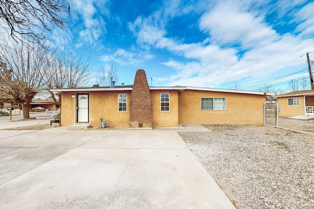 rear view of house featuring a chimney, fence, a gate, and stucco siding