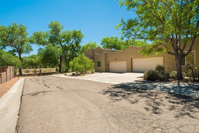 adobe home featuring a garage, driveway, fence, and stucco siding