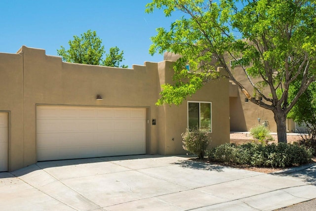 pueblo revival-style home featuring a garage, driveway, and stucco siding