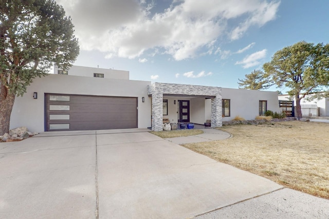 view of front of house with a garage, concrete driveway, stone siding, stucco siding, and a front yard