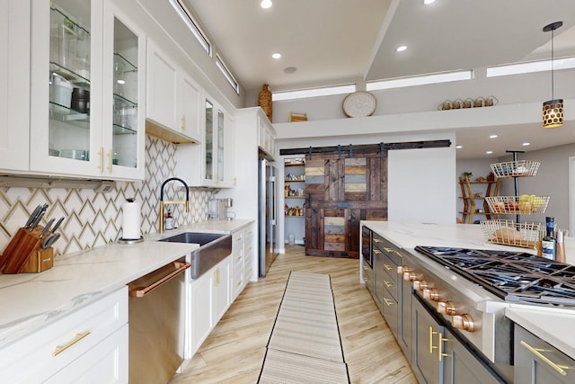 kitchen featuring a barn door, light wood-style flooring, stainless steel appliances, a sink, and white cabinets