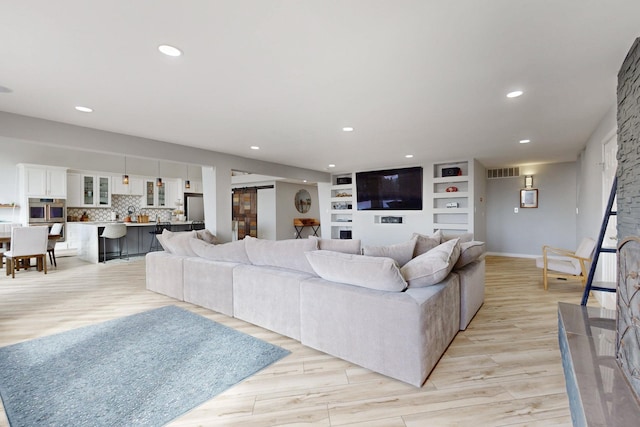 living room with light wood-style flooring, visible vents, baseboards, and recessed lighting