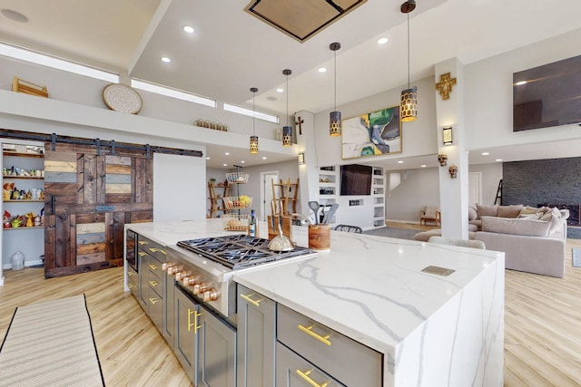 kitchen with a spacious island, a barn door, light wood-style floors, open floor plan, and gas cooktop