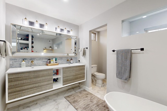 bathroom featuring double vanity, decorative backsplash, toilet, a soaking tub, and marble finish floor