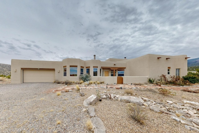 pueblo-style house with an attached garage, driveway, and stucco siding