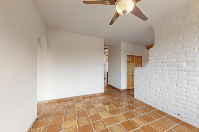 spare room featuring brick wall, ceiling fan, baseboards, and tile patterned floors