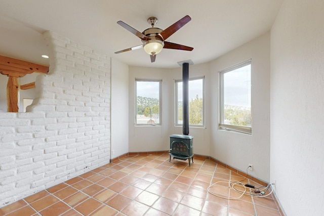 spare room with a ceiling fan, a wood stove, light tile patterned flooring, and brick wall