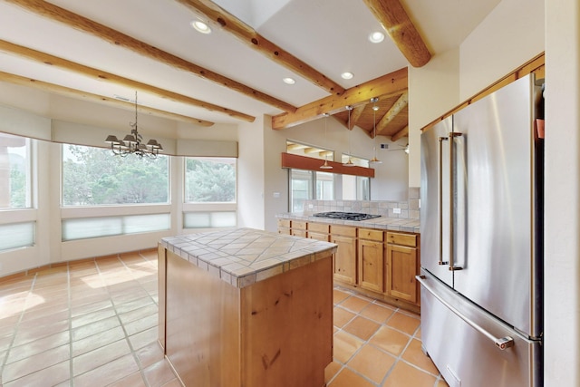 kitchen featuring tile countertops, backsplash, high end fridge, an inviting chandelier, and beam ceiling