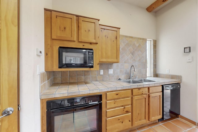 kitchen with light tile patterned floors, a sink, tile counters, black appliances, and tasteful backsplash