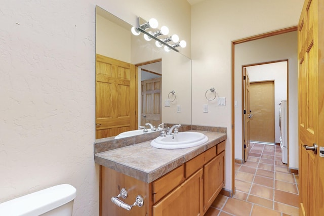 half bathroom with a textured wall, vanity, toilet, and tile patterned floors