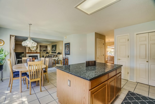 kitchen with a center island, brown cabinets, open floor plan, light tile patterned flooring, and a warm lit fireplace